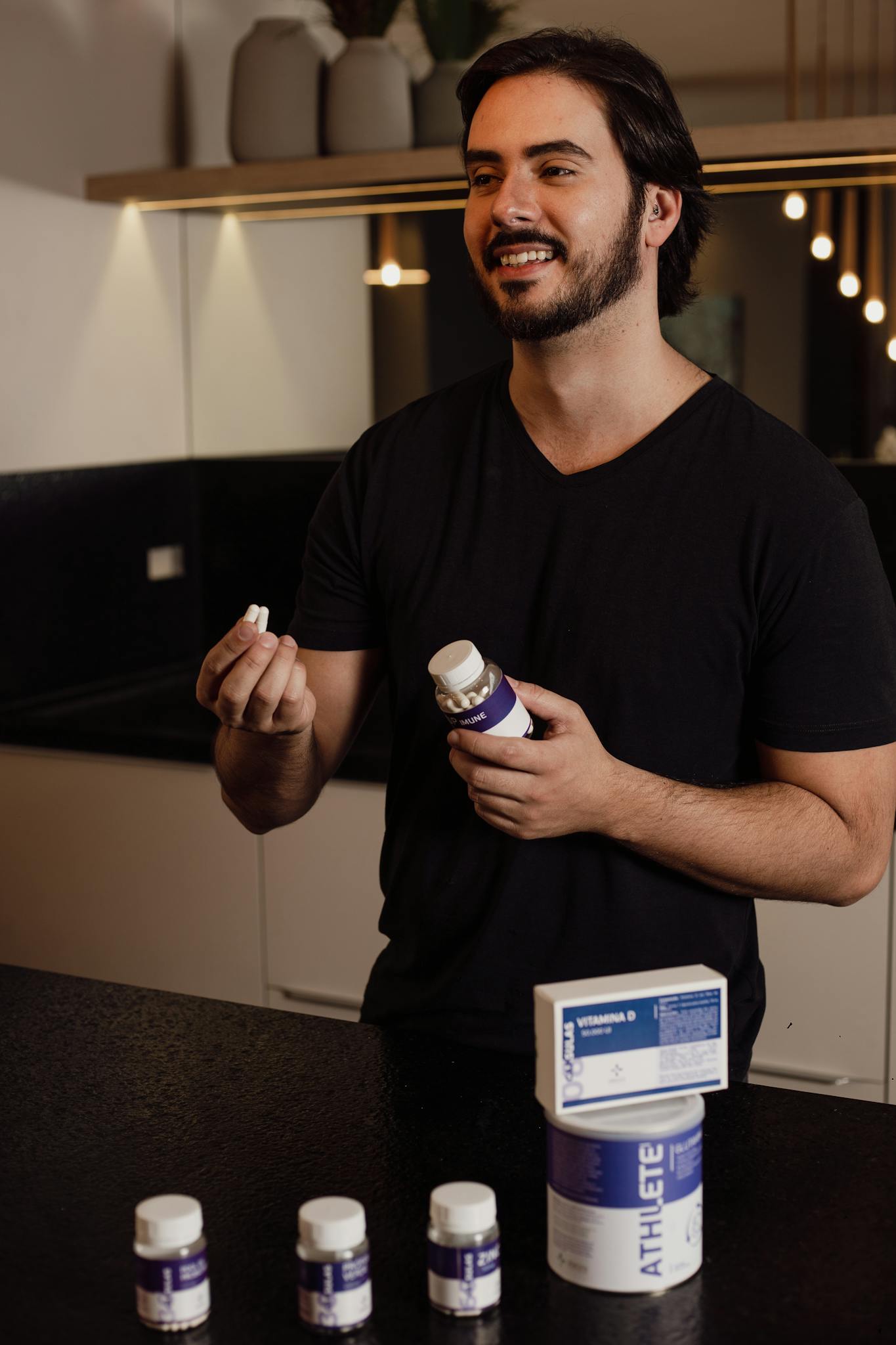 A cheerful man in a modern kitchen holding vitamin supplements, promoting health and wellness.