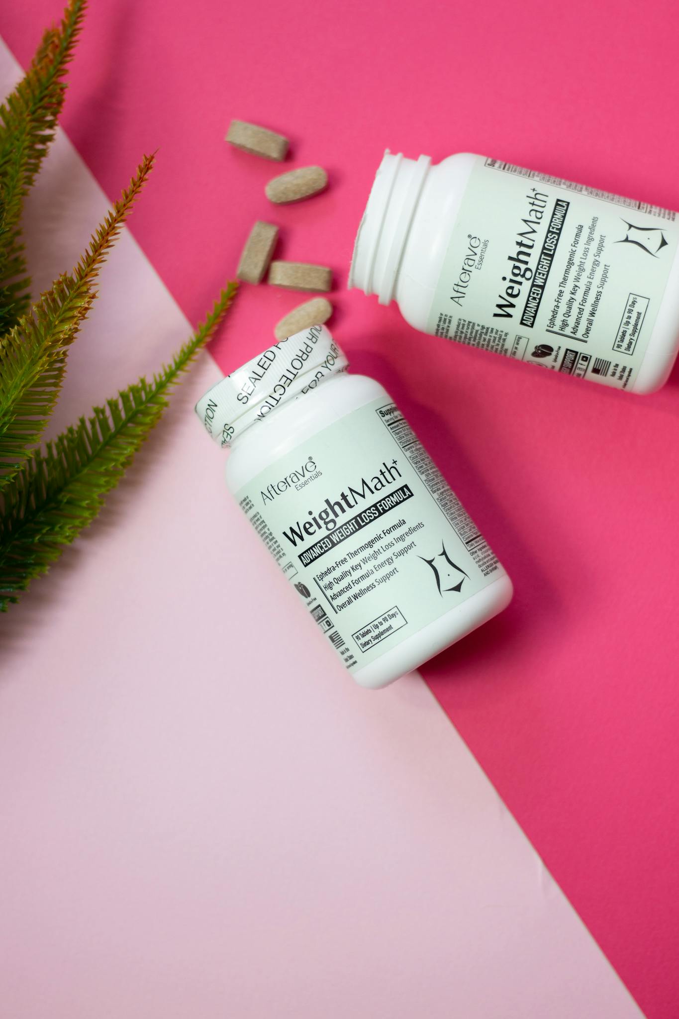 Two weight loss supplement bottles on a vibrant pink surface with scattered pills and greenery.