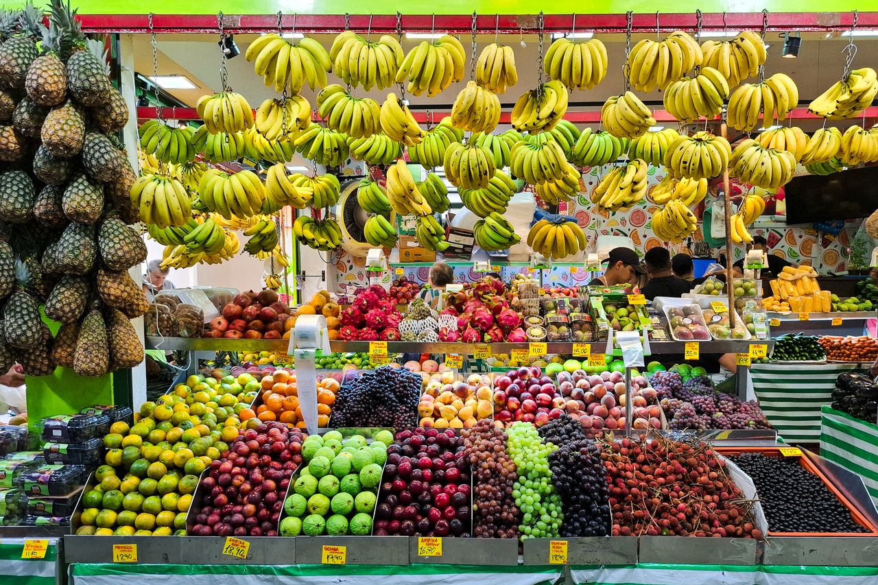 services-04 A colorful fruit market stall featuring an array of tropical fruits including bananas, pineapples, and apples.